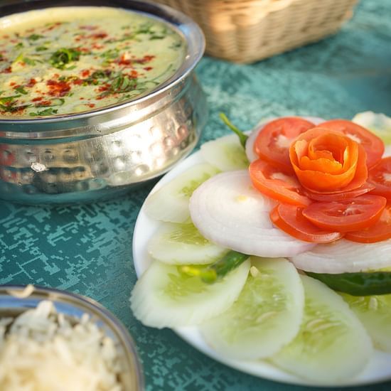A close up shot of a salad based out of tomatoes, onions and cucumber, along with a view of other dishes on the table